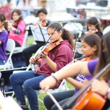 Middle school students play their instruments in an orchestra.