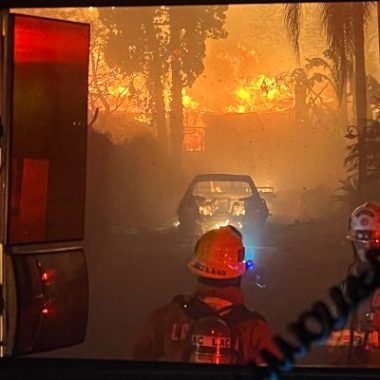 The back of a firefighter fighting a neighborhood wildfire.