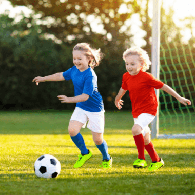 Two young kids are outside kicking a soccer ball.