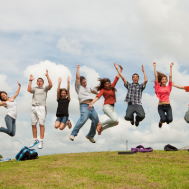 Teens jump in the air over a grassy field.