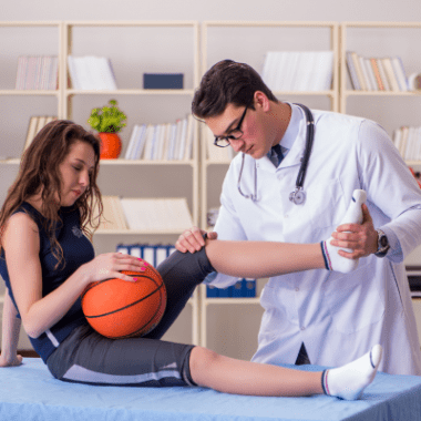 A doctor examines a teen girl's knee. She is holding a basketball.