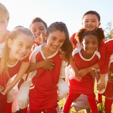 Girls and boys dressed in red and white sports clothes smile into the camera.