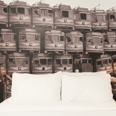 A wallpaper of red line buses frame a bed at The Redline Venice Hotel.